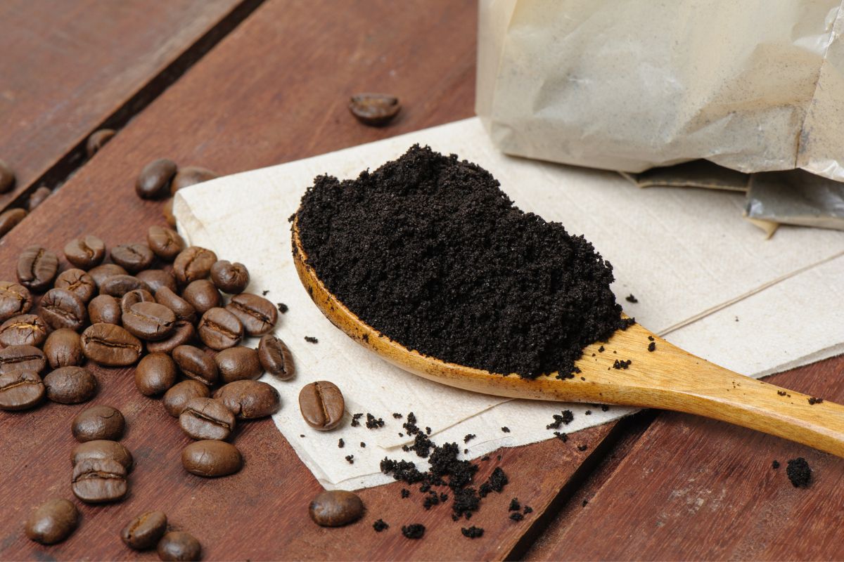 A wooden spoon full of coffee grounds on a wooden table with scattered coffee beans.