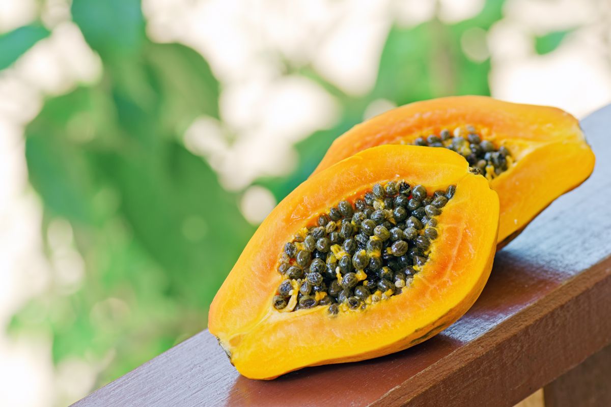 Two ripe halves of papaya on a wooden railing.