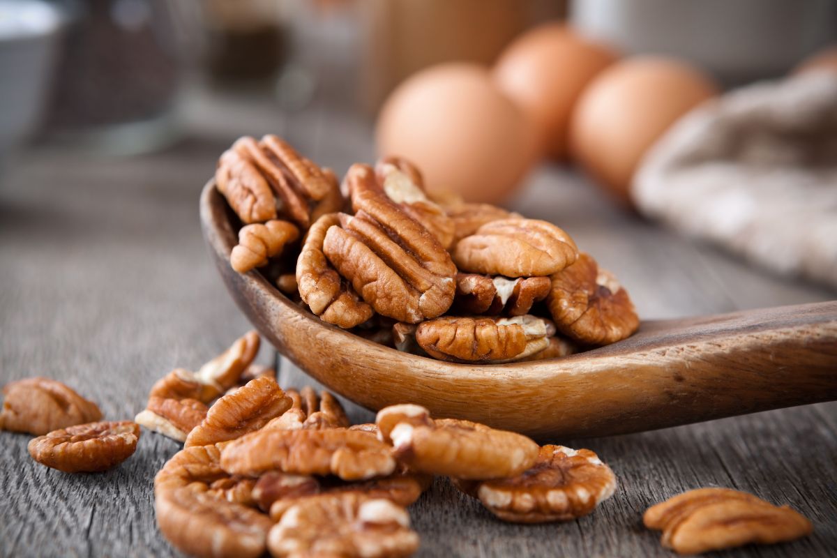 A close-up of a wooden spoon full of pecans on a wooden table.