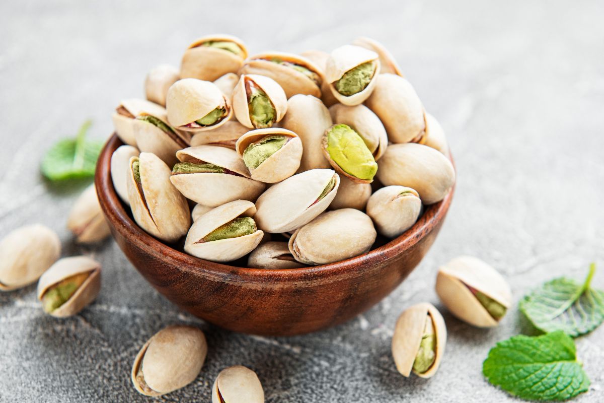 A wooden bowl of fresh pistachios on a table.