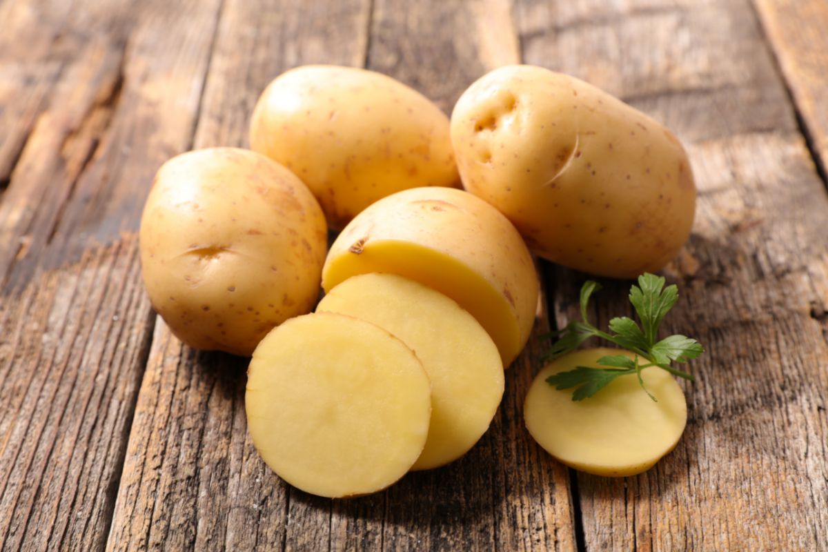 Whole and partially sliced organic potatoes on a wooden table.