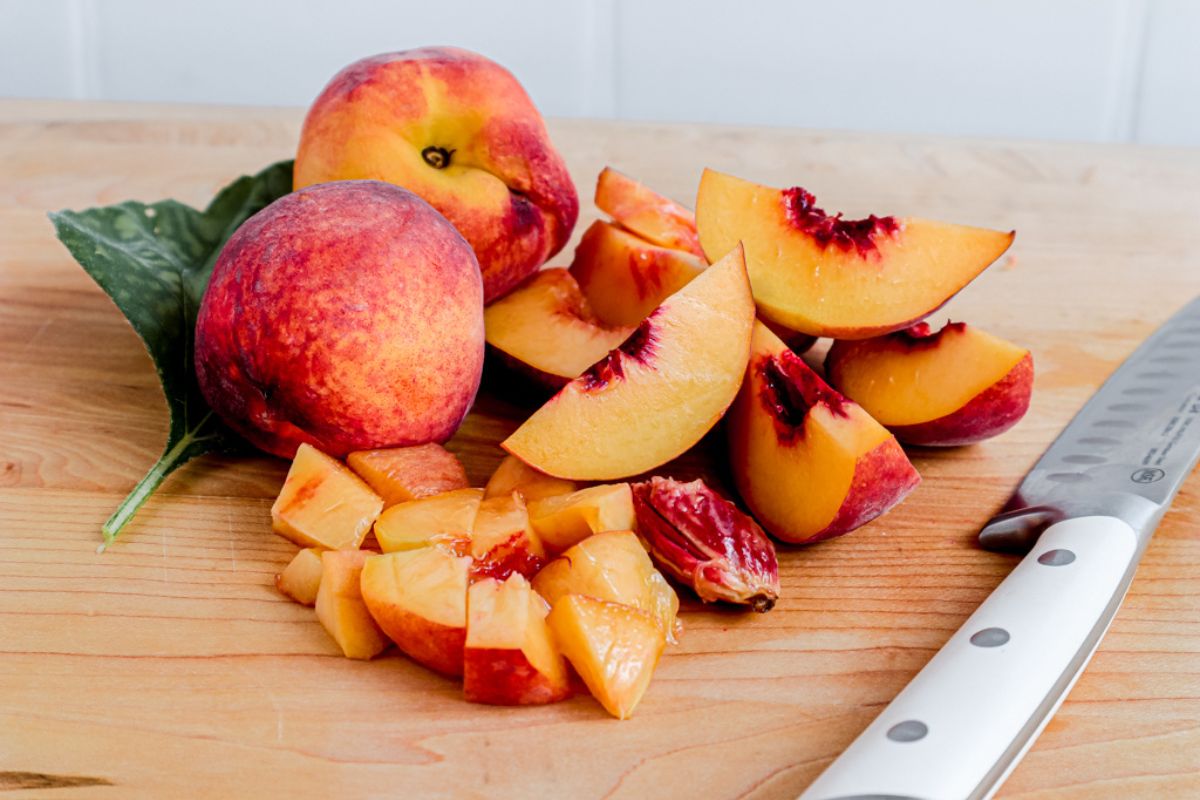 Whole and sliced ripe peaches on a wooden cutting board with a knife.