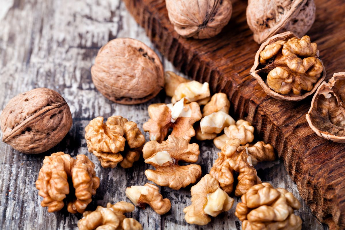 Whole and cracked walnuts on a wooden table.