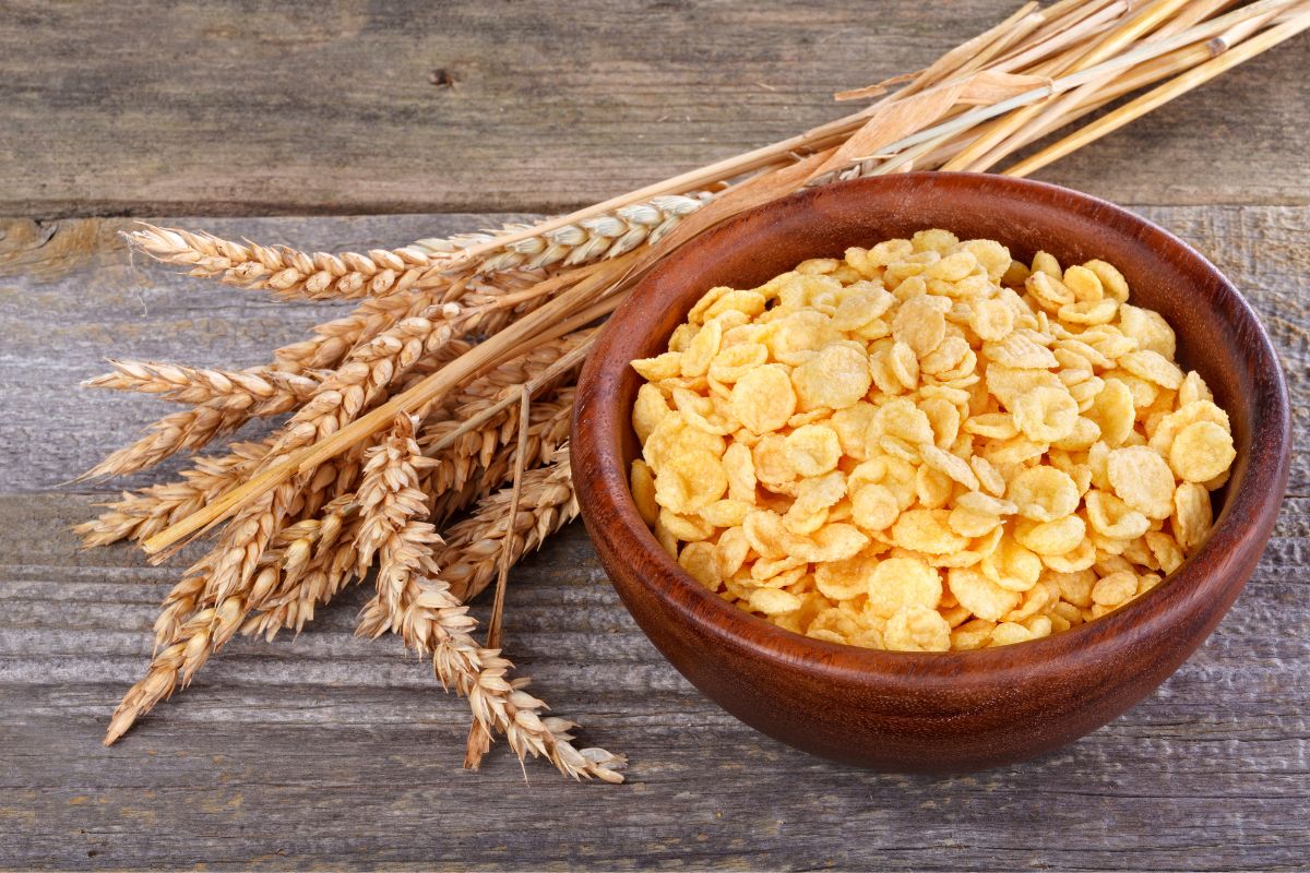 A wooden bowl of cereals on a wooden table with grain stalks.