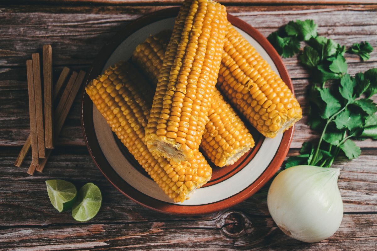 A plate full of corn cobs on a table with other varieties of vegetables.