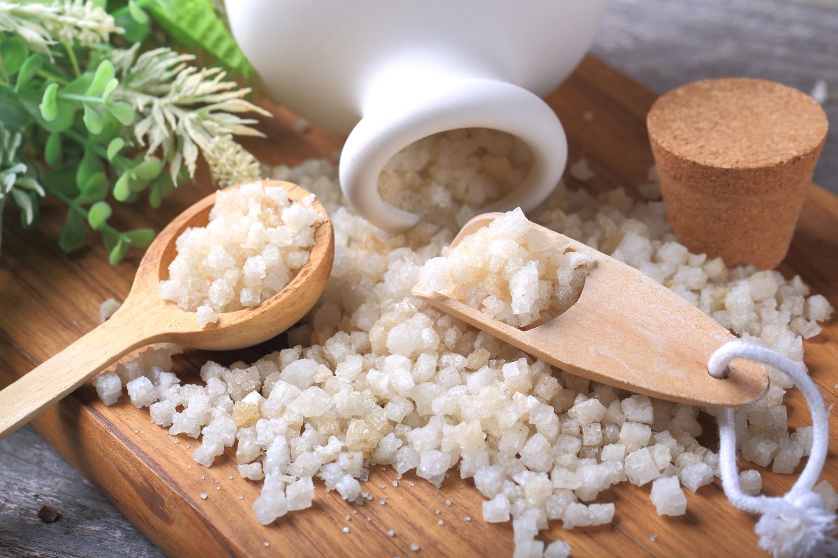 Epsom salt spilled from a container on a wooden board and a wooden spoon.