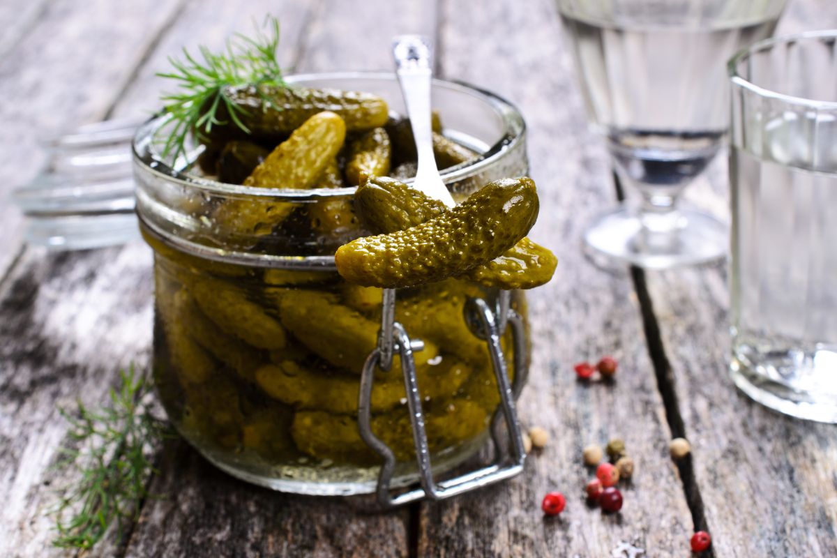 A glass jar of pickles with a fork on a wooden table.