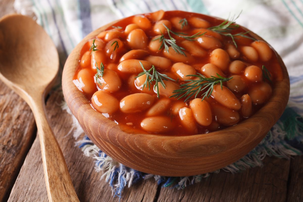 A wooden bowl of baked beans on a wooden table.
