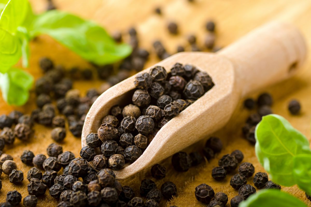 A wooden scoop of black pepper on a wooden table.