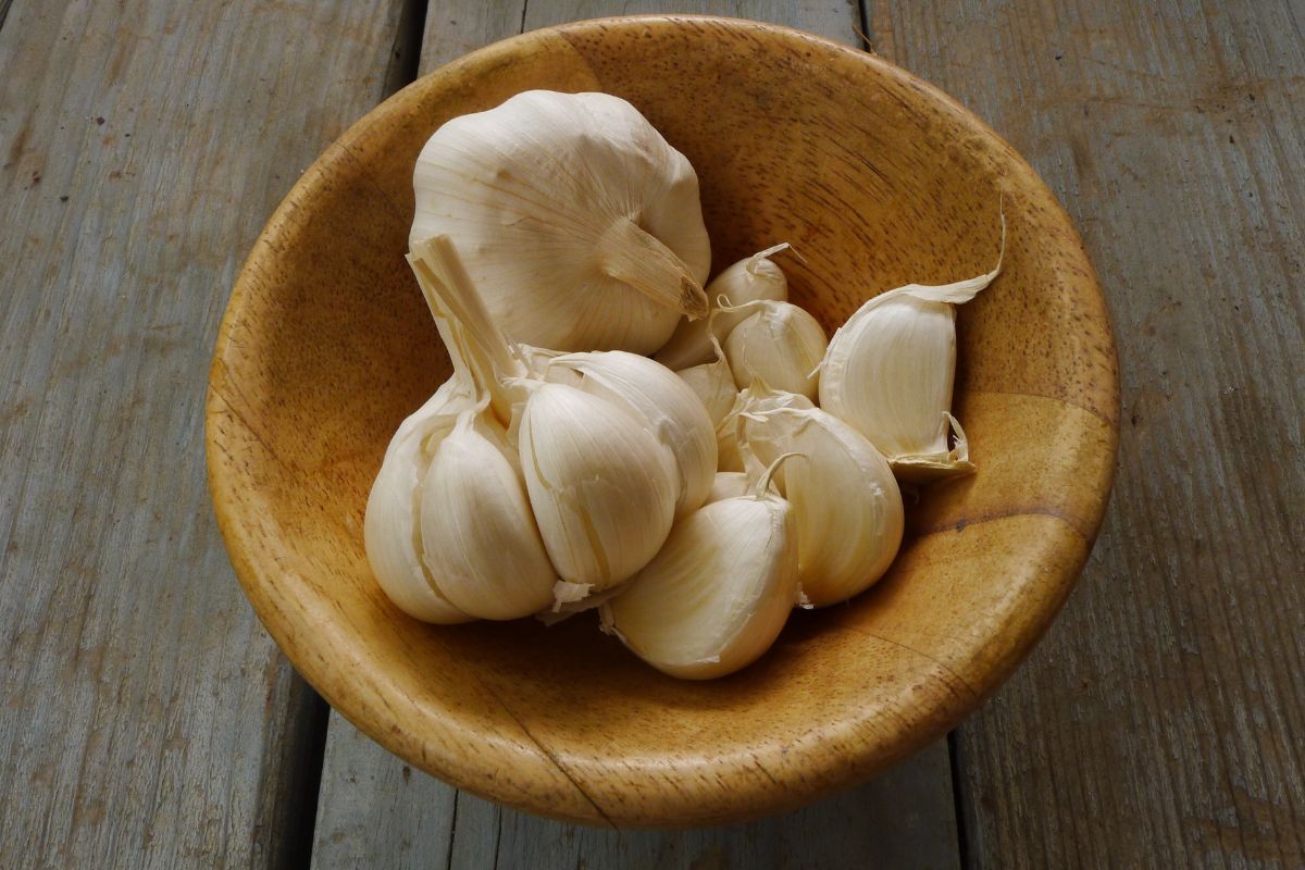 A wooden bowl with cloves of garlic on a wooden table.