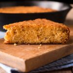A piece of freshly baked cornbread on a wooden cutting board.