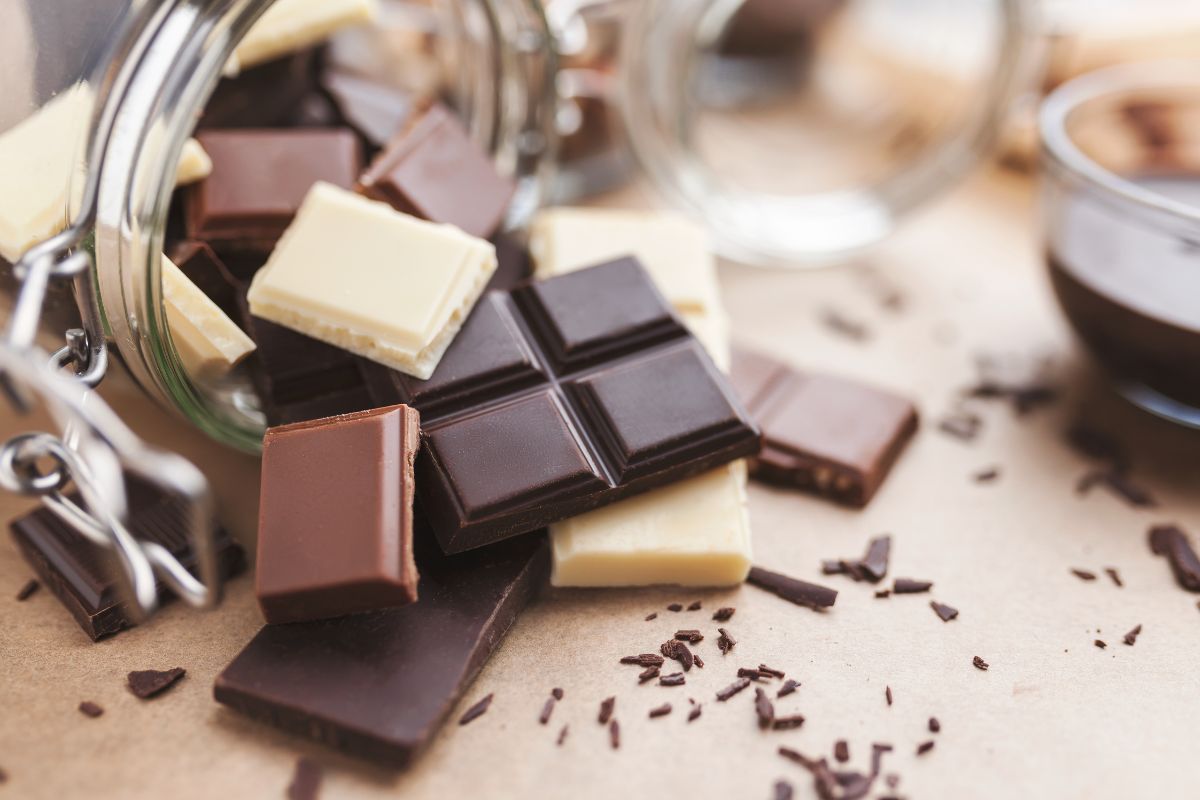 Different varieties of chocolate bars spilled on a table from a glass jar.