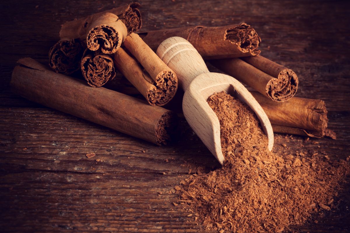 A wooden scoop of cinnamon and cinnamon rolls on a wooden table.