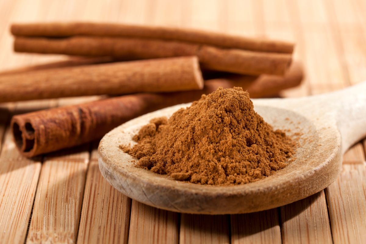 A wooden spoon of cinnamon and cinnamon rolls on a wooden table.