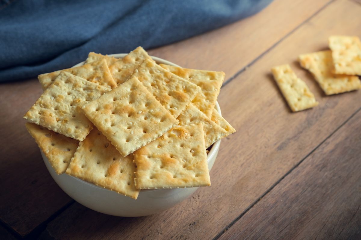A white bowl full of crackers on a wooden table.
