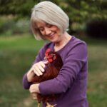 An older woman holding and petting a chicken.