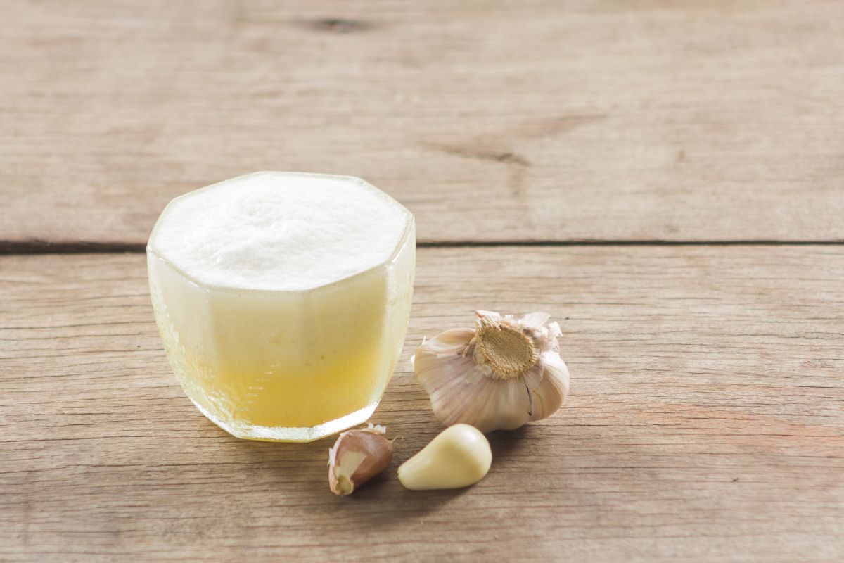 A glass of garlic juice with cloves of garlic on a wooden table.