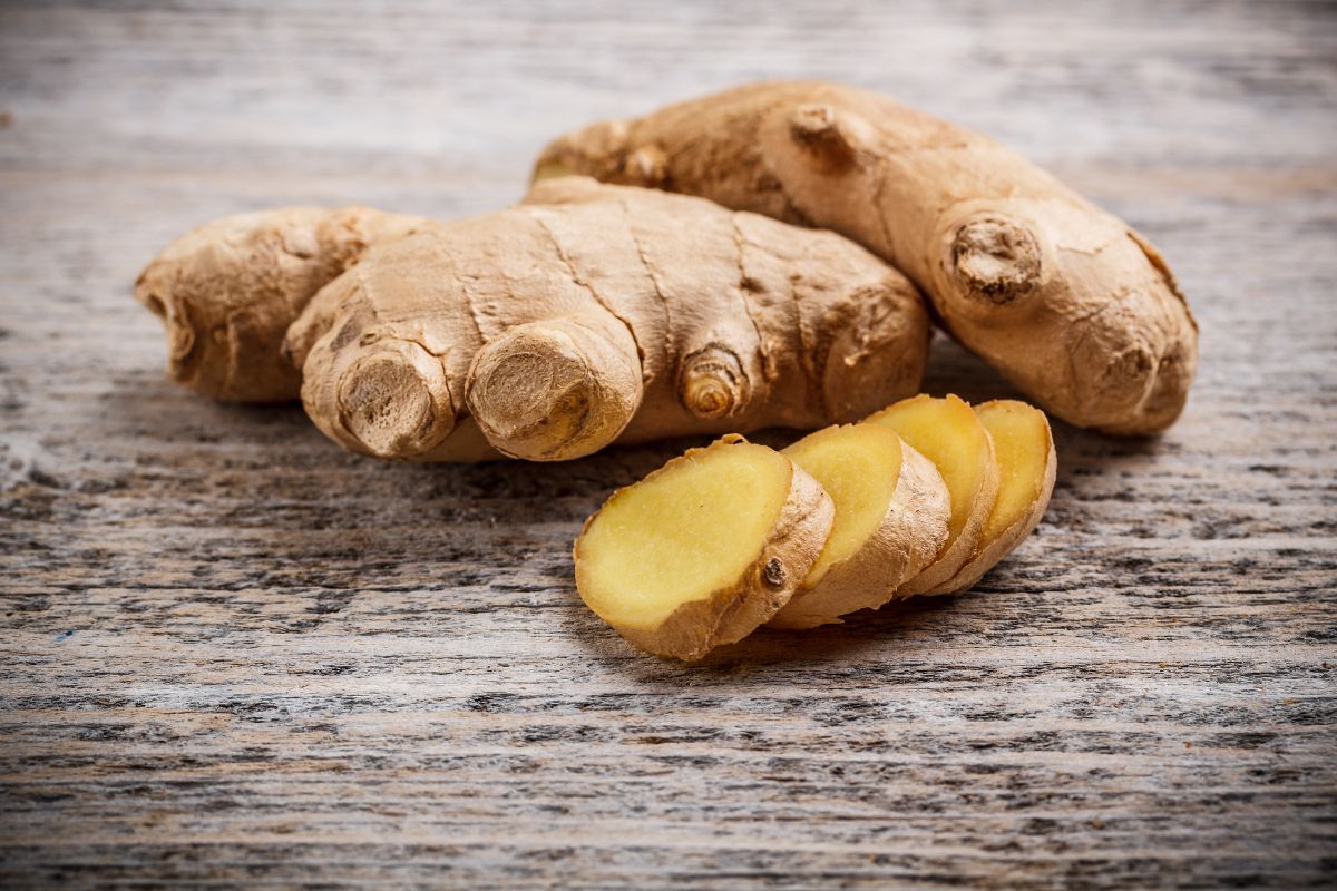 Whole and sliced ginger on a wooden table.