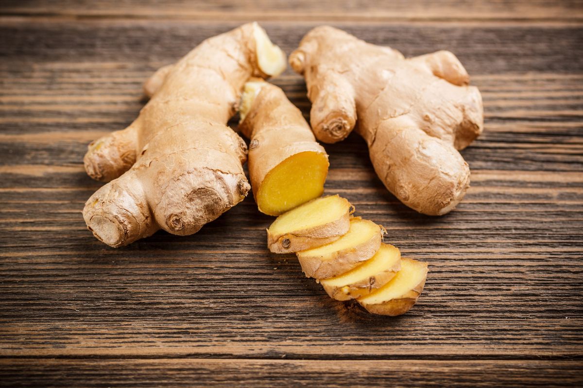 Whole and sliced ginger root on a wooden table.