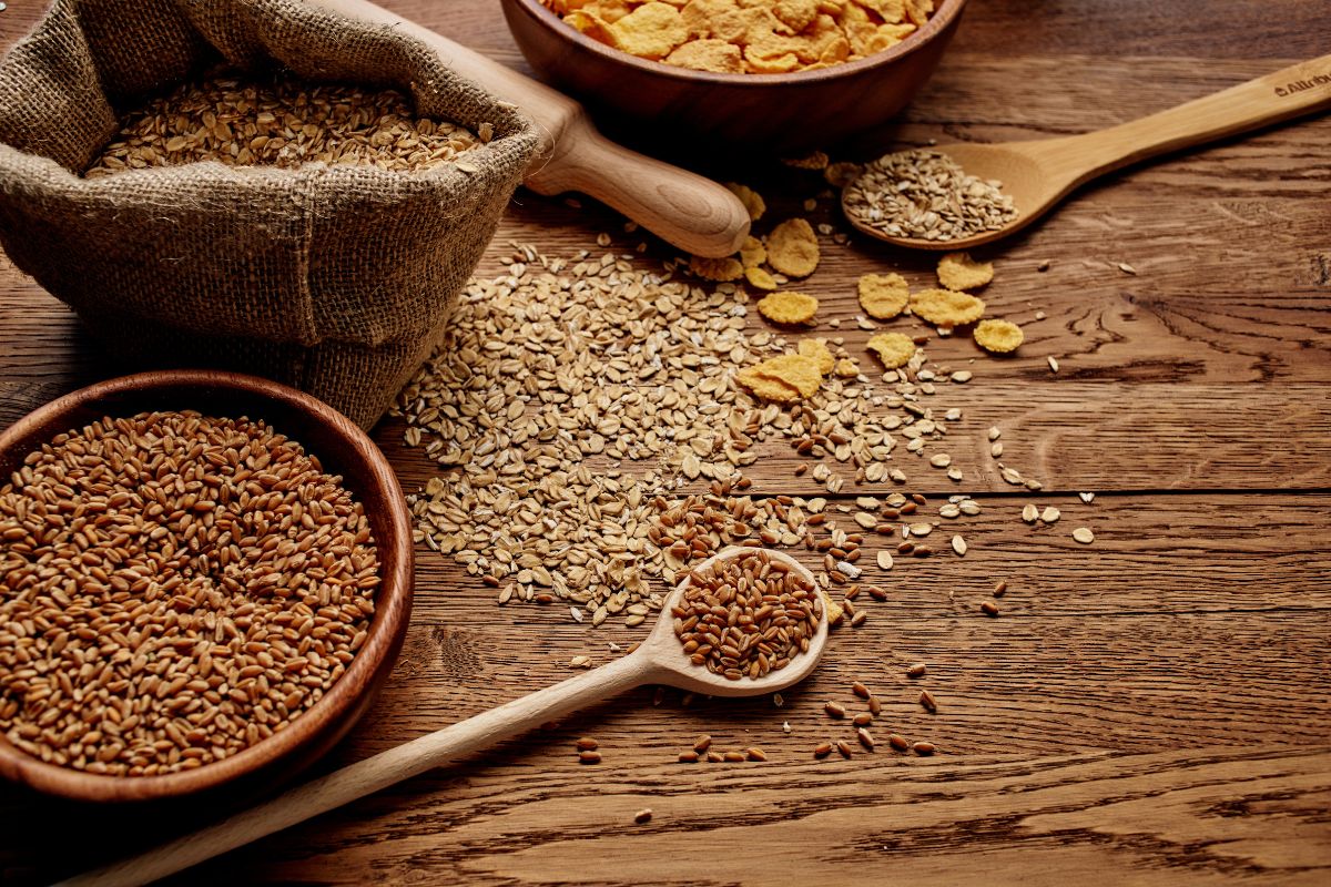 Different varieties of grains are in a sack and bowls on a wooden table.