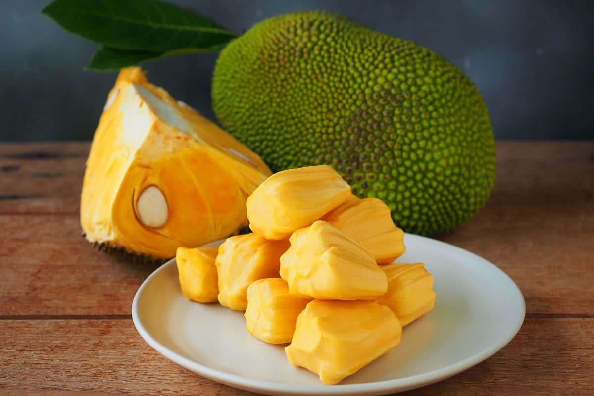 Sliced jackfruits on a white plate on a wooden table with the rest of jackfruits.