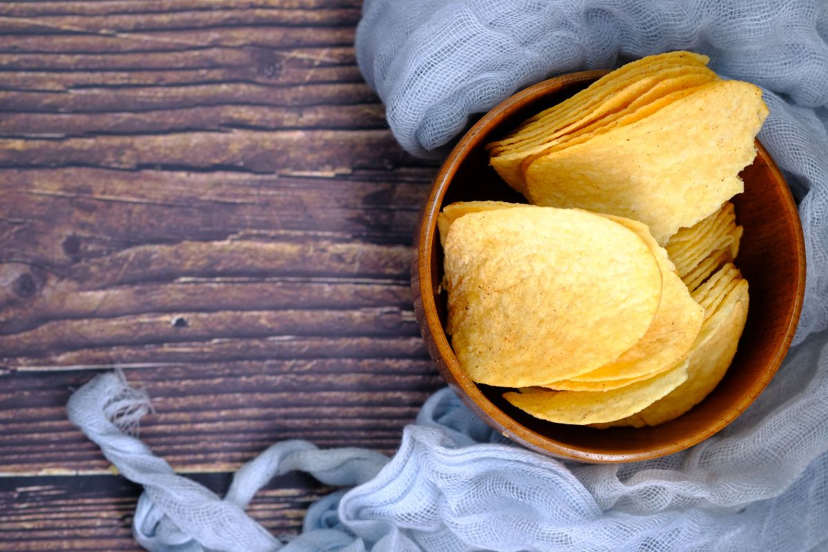 A wooden bowl of potato chips on a wooden table.