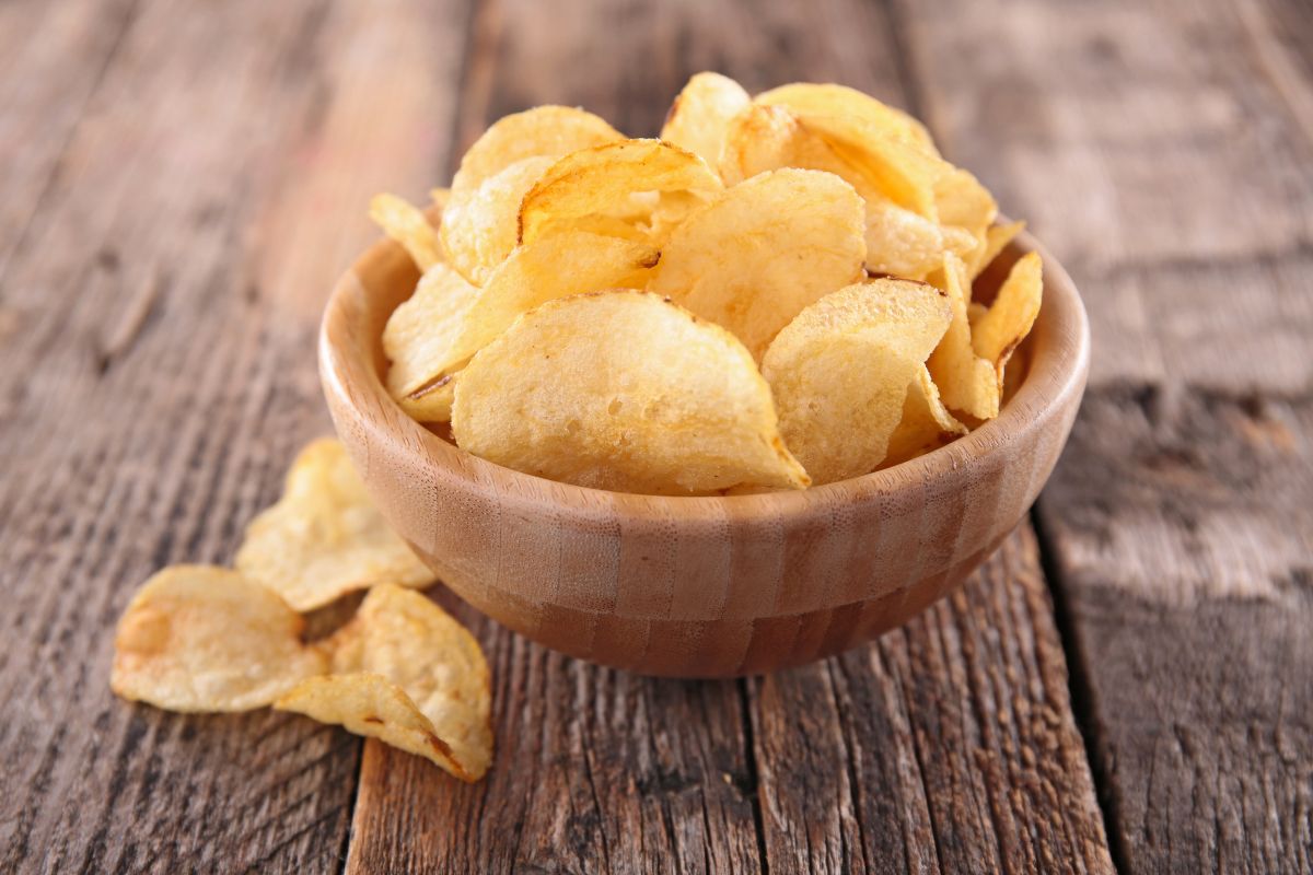 A wooden bowl of potato chips on a wooden table.