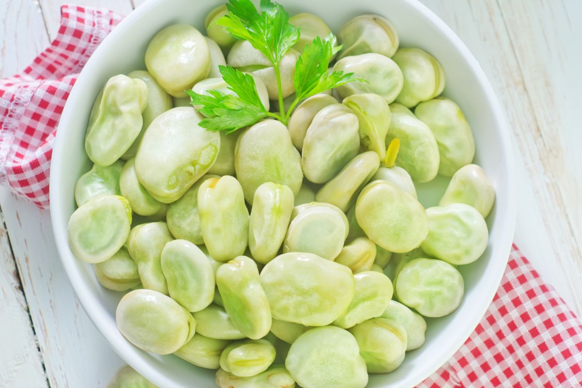 A white bowl full of raw green beans on a table.