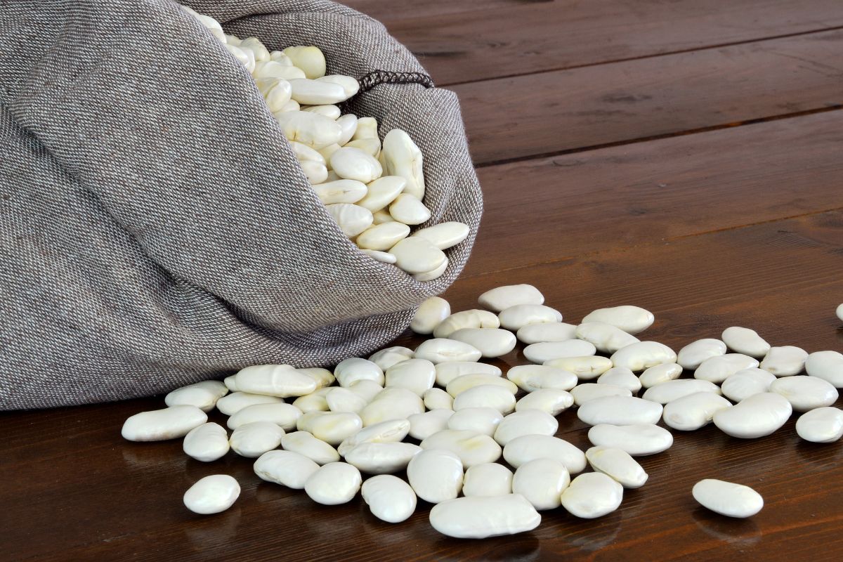 A sack of lima beans spilled on a wooden table.