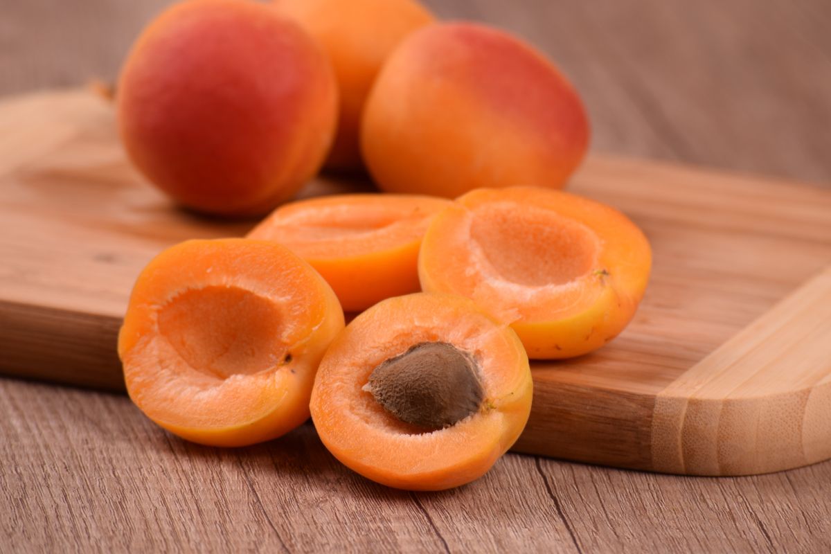 Whole and sliced apricots on a wooden cutting board.