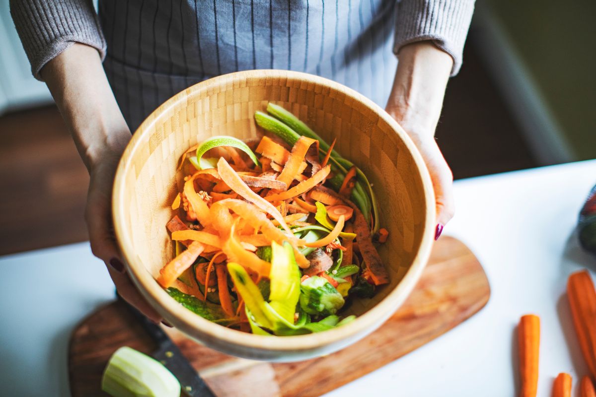 Hands are holding a wooden bowl with vegetable leftovers.