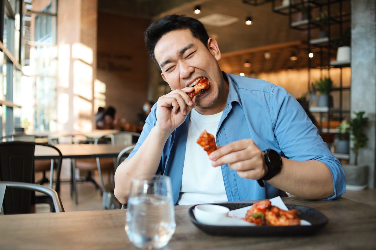 Young man eating chicken wings in a restaurant