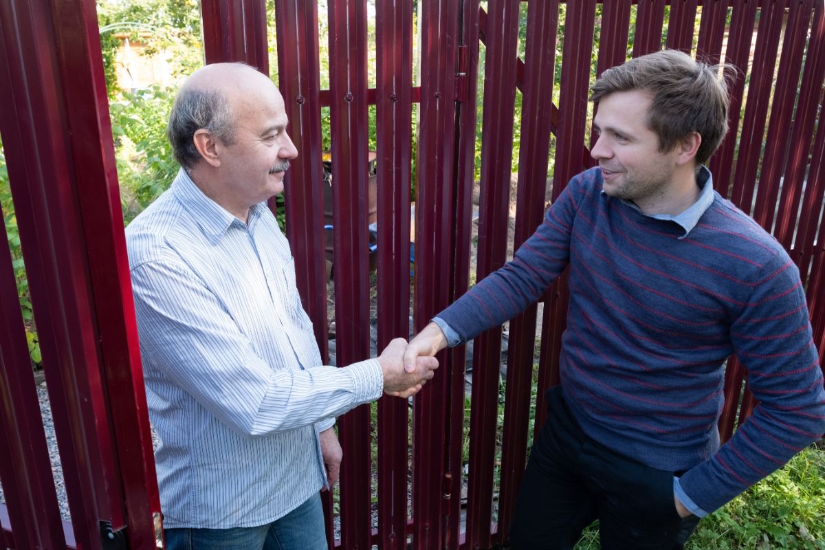 Two neighbors shaking hands near a fence