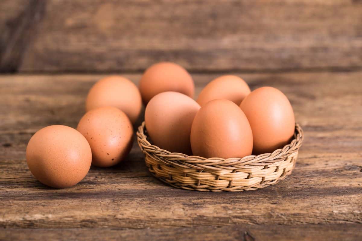 A bunch of organic chicken eggs in a small basket and on a wooden table.